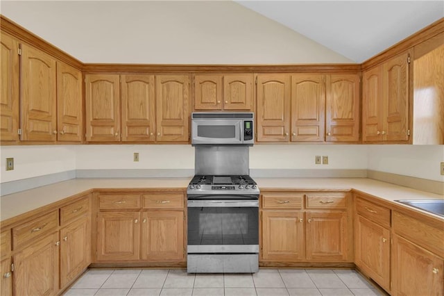 kitchen with light tile patterned flooring, stainless steel appliances, sink, and vaulted ceiling