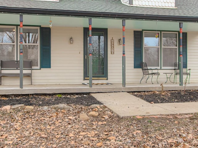 doorway to property featuring covered porch and a shingled roof