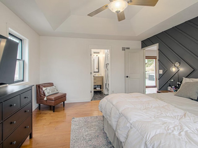 bedroom featuring ceiling fan, a tray ceiling, ensuite bath, and light hardwood / wood-style flooring