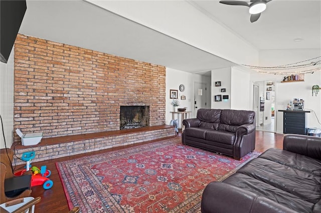 living area featuring wood finished floors, a fireplace, brick wall, and a ceiling fan