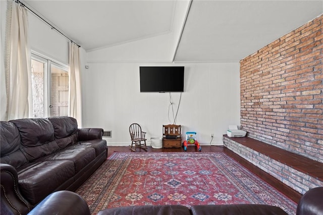 living area featuring lofted ceiling, wood finished floors, visible vents, and brick wall