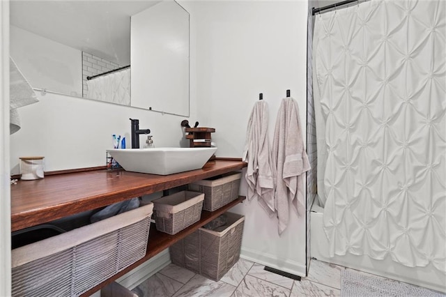 full bathroom with a sink, shower / bath combo with shower curtain, and marble finish floor