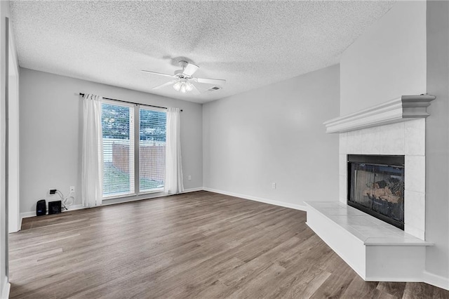 unfurnished living room featuring a textured ceiling, wood-type flooring, a tile fireplace, and ceiling fan