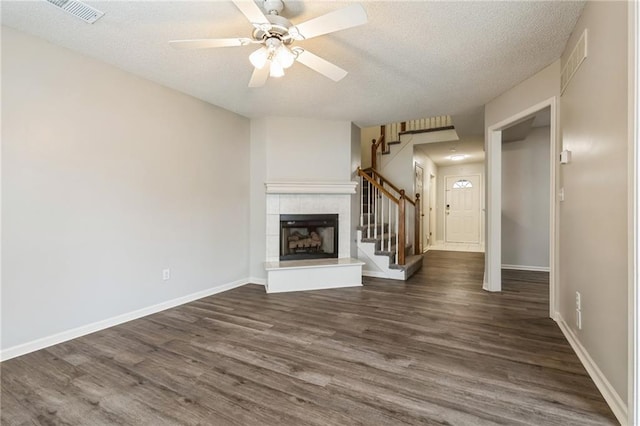 unfurnished living room with a tiled fireplace, ceiling fan, dark wood-type flooring, and a textured ceiling