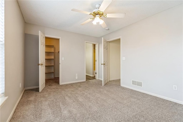 unfurnished bedroom featuring a spacious closet, light colored carpet, ceiling fan, and a closet