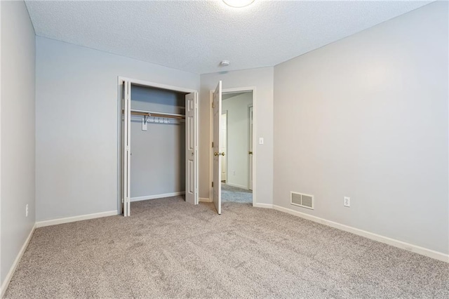 unfurnished bedroom featuring light colored carpet, a textured ceiling, and a closet