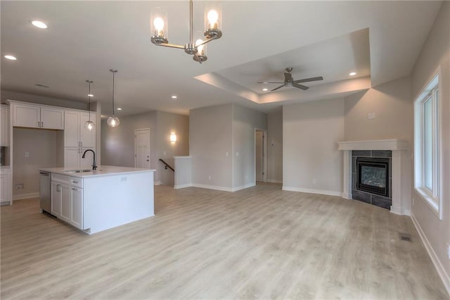 kitchen featuring white cabinetry, stainless steel dishwasher, light wood-style flooring, a sink, and ceiling fan with notable chandelier