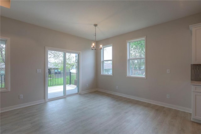 unfurnished dining area with a notable chandelier, baseboards, and light wood-type flooring