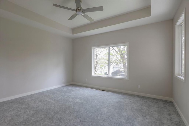 empty room featuring a ceiling fan, a raised ceiling, a healthy amount of sunlight, and carpet floors