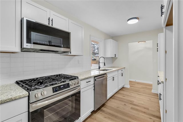 kitchen featuring stainless steel appliances, white cabinetry, sink, and light stone counters