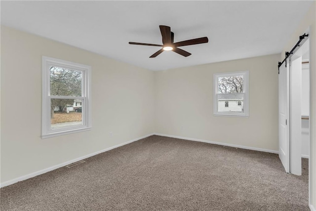 carpeted empty room with a barn door and ceiling fan