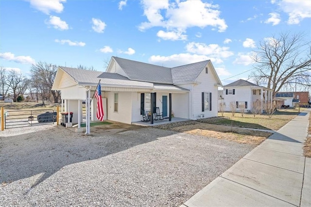 view of front of property featuring gravel driveway, covered porch, an attached garage, and fence