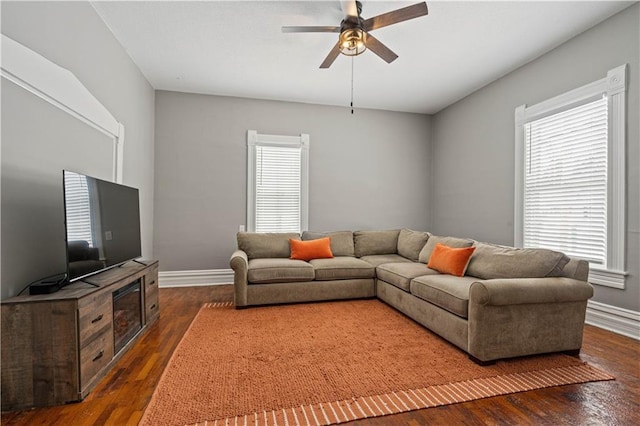 living room with dark wood-type flooring, ceiling fan, and baseboards