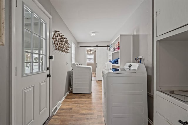 laundry room with laundry area, a barn door, visible vents, wood finished floors, and independent washer and dryer