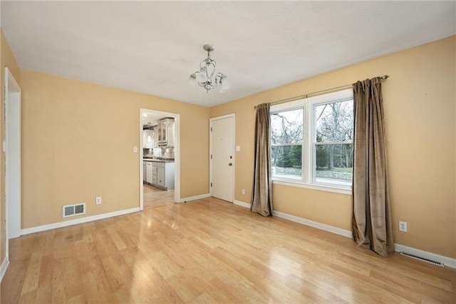 spare room with a chandelier and light wood-type flooring