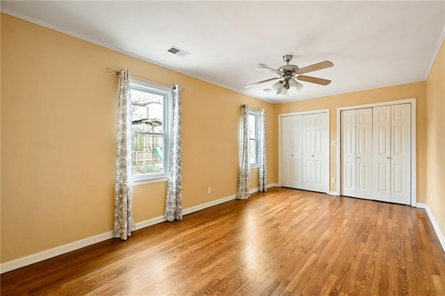 unfurnished bedroom with hardwood / wood-style floors, multiple closets, and ceiling fan