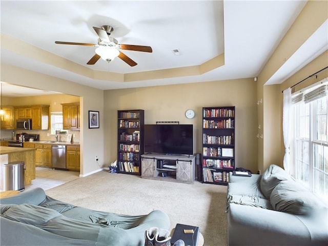 living room with light carpet, ceiling fan, and a tray ceiling