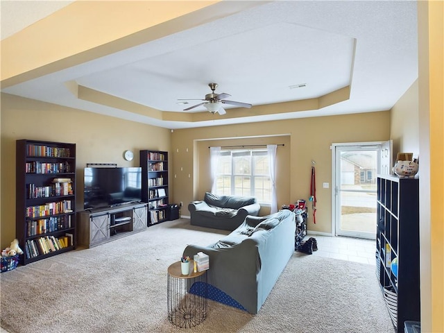 living room featuring ceiling fan, light colored carpet, and a tray ceiling