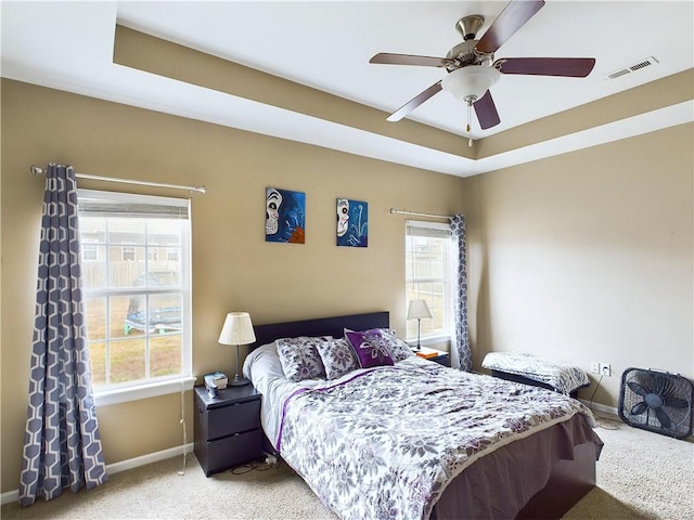 carpeted bedroom featuring multiple windows, a raised ceiling, and ceiling fan