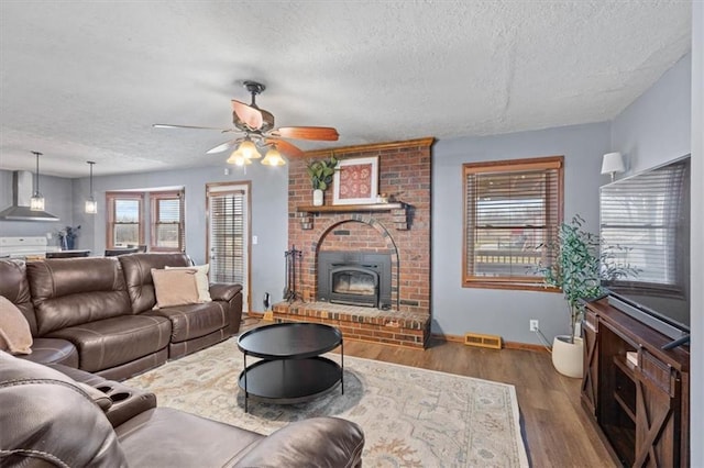 living room featuring ceiling fan, a fireplace, dark hardwood / wood-style floors, and a textured ceiling