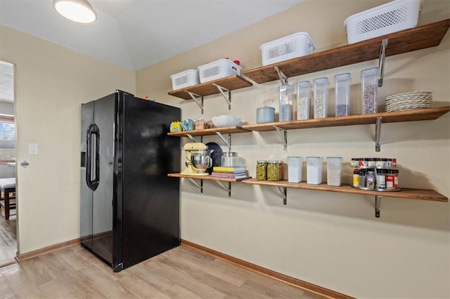 kitchen featuring black refrigerator with ice dispenser, light hardwood / wood-style floors, and vaulted ceiling