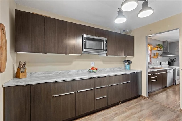 kitchen featuring stainless steel appliances, wall chimney range hood, dark brown cabinetry, and light hardwood / wood-style floors