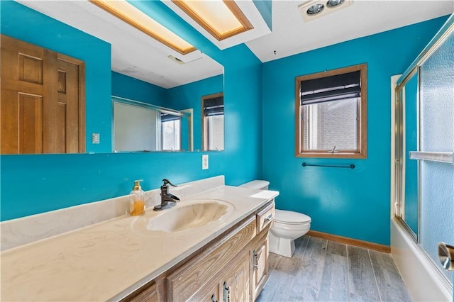 full bathroom with vanity, hardwood / wood-style floors, bath / shower combo with glass door, and toilet