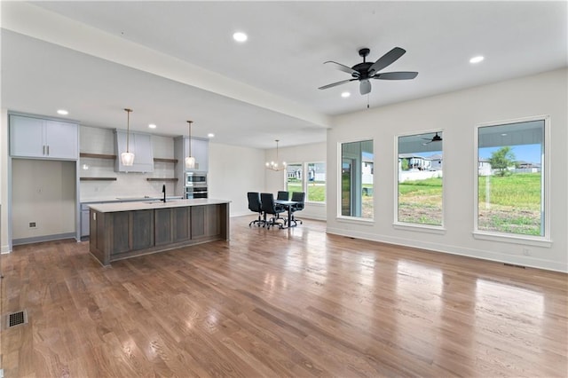 kitchen featuring wood-type flooring, sink, backsplash, hanging light fixtures, and a kitchen island with sink