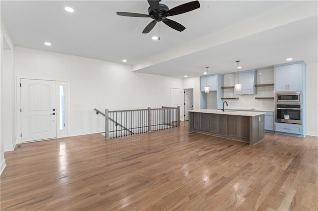 kitchen featuring stainless steel appliances, an island with sink, light wood-type flooring, and decorative light fixtures