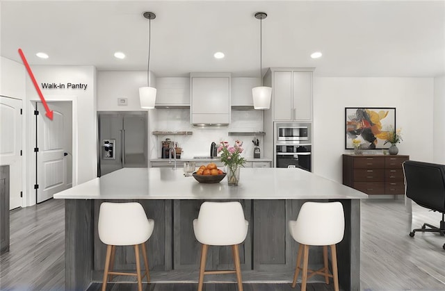 kitchen with stainless steel appliances, light countertops, light wood-type flooring, backsplash, and a large island with sink