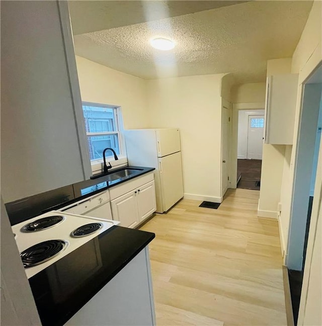 kitchen featuring sink, white refrigerator, a textured ceiling, white cabinets, and light wood-type flooring