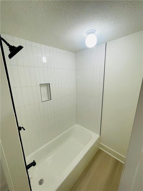 bathroom with tiled shower / bath combo, wood-type flooring, and a textured ceiling