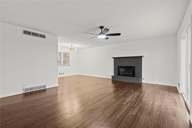 unfurnished living room featuring dark hardwood / wood-style flooring, ceiling fan with notable chandelier, a fireplace, and plenty of natural light