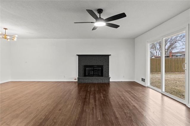 unfurnished living room featuring hardwood / wood-style flooring, a brick fireplace, ceiling fan with notable chandelier, and a textured ceiling