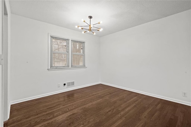 spare room featuring a notable chandelier, dark wood-type flooring, and a textured ceiling