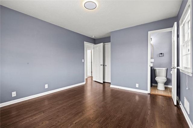 unfurnished bedroom featuring ensuite bathroom and dark hardwood / wood-style floors