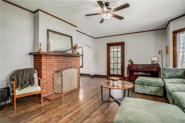 living room with a brick fireplace, dark wood-type flooring, ornamental molding, and ceiling fan