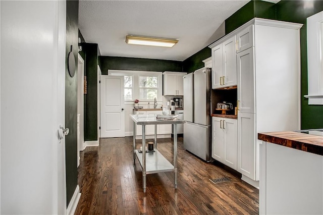 kitchen with white cabinetry, dark hardwood / wood-style flooring, stainless steel refrigerator, and butcher block countertops