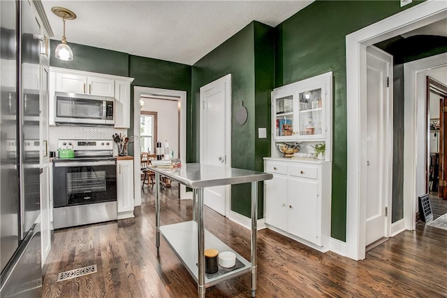 kitchen with pendant lighting, stainless steel appliances, dark hardwood / wood-style floors, and white cabinets