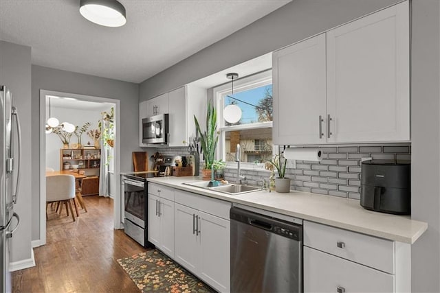 kitchen with stainless steel appliances, white cabinetry, sink, and dark hardwood / wood-style flooring