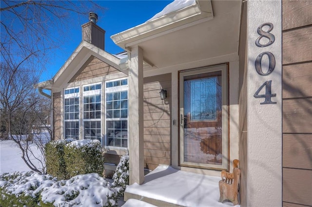 snow covered property entrance with a chimney