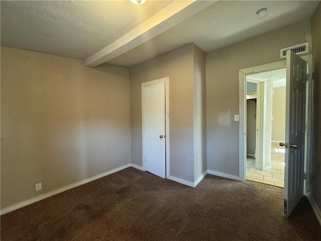 unfurnished bedroom with beam ceiling, a textured ceiling, and dark carpet