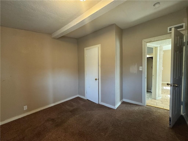 unfurnished bedroom with beam ceiling, a textured ceiling, and dark colored carpet