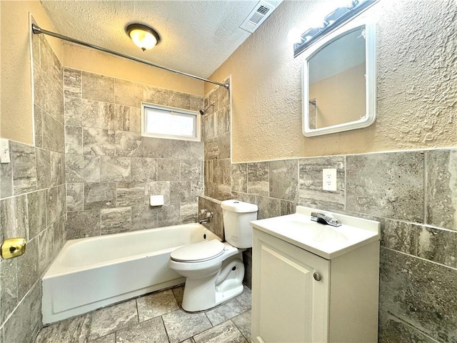 full bathroom with tile walls, tiled shower / bath combo, vanity, toilet, and a textured ceiling