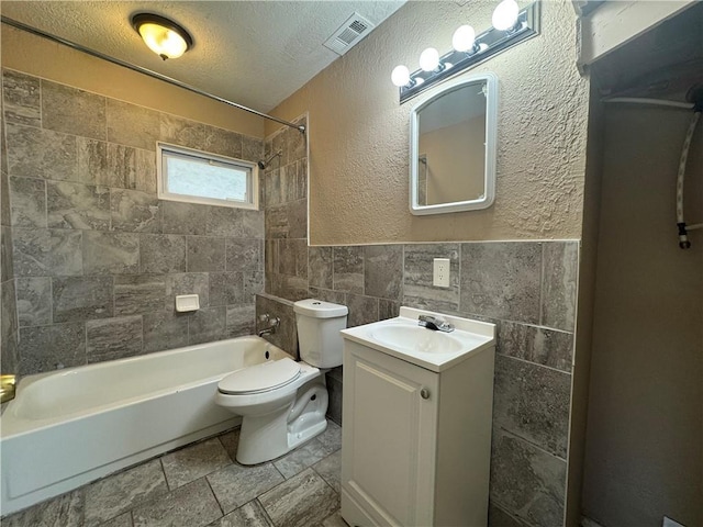 full bathroom with tile walls, tiled shower / bath combo, vanity, toilet, and a textured ceiling