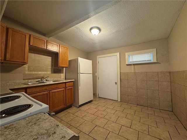 kitchen featuring sink, a textured ceiling, light tile patterned floors, tile walls, and white appliances