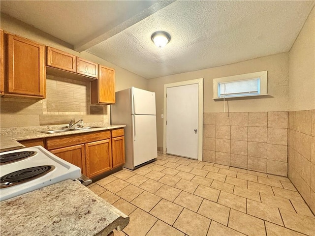 kitchen featuring sink, white appliances, tile walls, a textured ceiling, and light tile patterned flooring