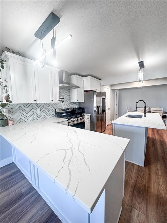 kitchen with pendant lighting, sink, kitchen peninsula, stainless steel appliances, and wall chimney range hood