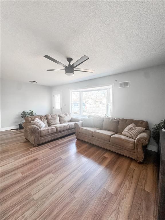 living room featuring ceiling fan, light hardwood / wood-style flooring, and a textured ceiling