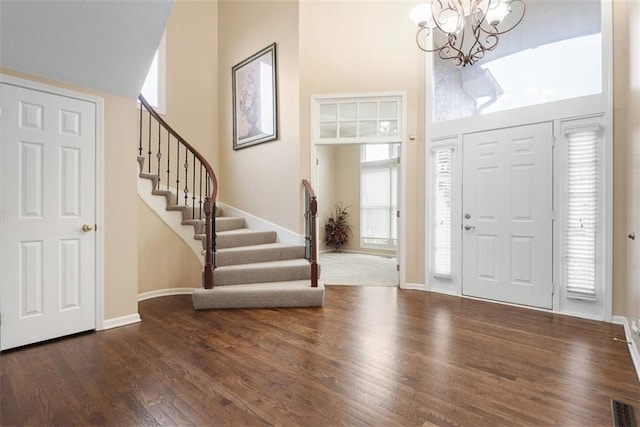 foyer entrance with an inviting chandelier, a towering ceiling, and dark hardwood / wood-style floors